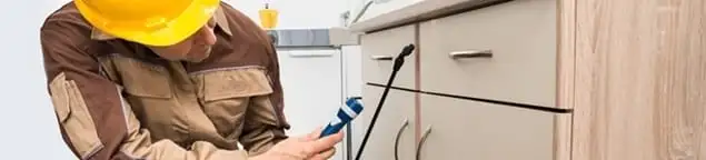Roach exterminator applying treatment under kitchen cabinets in Orlando, FL