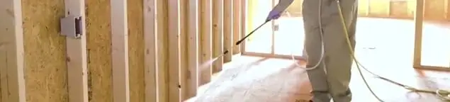 Termite treatment technician applying spray along framing and unfinished walls in Orlando, FL